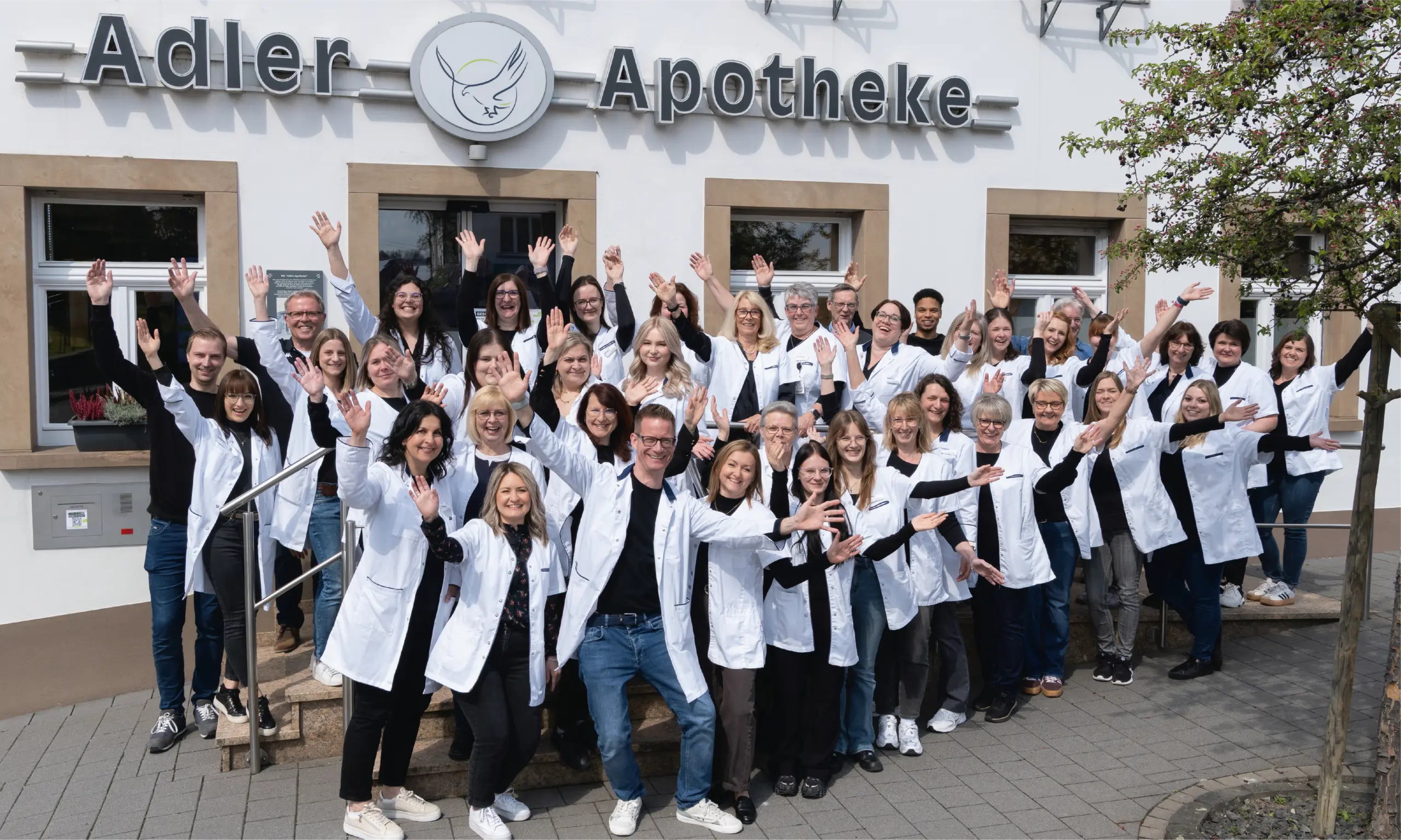 Team der Adler Apotheke Rhaunen fröhlich winkend vor der Apotheke