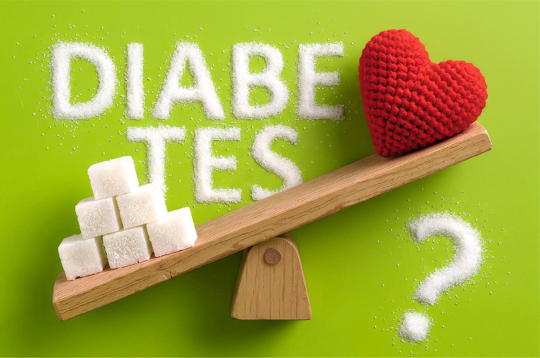 Wippe auf der Zuckerwürfel und ein gehäckeltes Herz liegen. Die Zuckerwürfel kippen die Wippe zu ihren Guntsten nach unten und das Herz ist oben. Im Hintergrund steht mit Zucker geschrieben: Diabetes?